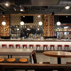 This image shows a modern bar area at Punch Bowl Social Atlanta, featuring circular light fixtures and stylish red bar stools. The decor blends industrial elements with warm lighting and sleek seating.