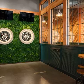 This image shows the dartboard area at Punch Bowl Social Atlanta, with greenery wall decor and a cozy atmosphere. The combination of natural and industrial elements adds to the playful vibe of the space.