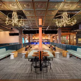 This photo features the stylish bowling lanes at Punch Bowl Social Atlanta, highlighted by neon chandeliers and intricately designed ceiling tiles. The space combines fun and elegance, creating a unique entertainment experience.