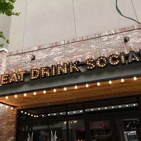 This close-up shot highlights the entrance to Punch Bowl Social in Atlanta, with its illuminated 'Eat Drink Social' sign. The warm lighting and rustic brickwork create an inviting ambiance for guests.