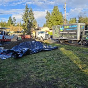 Kaizen Plumbing service trucks and excavation equipment at a residential site.