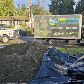 Kaizen Plumbing trucks and excavation equipment in a residential area.