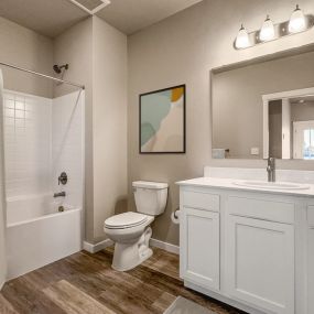 Bathroom with plank flooring, white vanity area, and square tiled shower area with tub