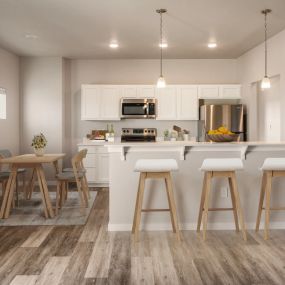 View of kitchen with white cabinetry and recessed lighting, counter area with bar stools and pendant lighting, and dining room table and chairs to the left