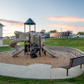 Playground at dusk complete with two slides, a set of stairs, and a park bench surrounded by a grassy hill