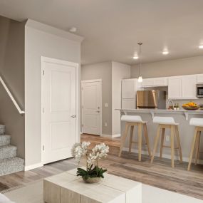 View from living room into kitchen with contemporary coffee table, plank flooring, view of barstool counter seating across from the kitchen area, and side view of stairs leading up to bedrooms