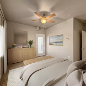 Cozy bedroom with neutral bedding, ceiling fan, and opposite wall with a neutral wood dresser and mirror with a door leading to an outdoor space