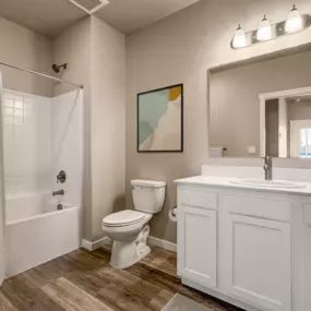 Bathroom with plank flooring, white vanity area, and square tiled shower area with tub