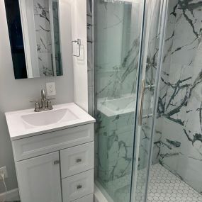 beautifully remodeled walk in shower with custom tile surround, tile flooring and a frameless glass shower door.