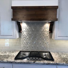 Range with white patinaed cabinets, granite countertops, and Flower of Life textured backsplash for a stylish and artistic kitchen.