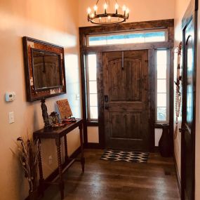 A front entranceway adorned with dark wood floors, door, and trim. A captivating hanging light fixture illuminates the space, casting a warm and inviting glow, while the dark wood elements create a sense of elegance and sophistication.