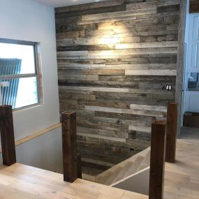 A staircase with a gray restored barnwood wall, adding a touch of rustic charm. The reclaimed barnwood brings a unique texture to the space, creating a focal point that combines the beauty of nature with a modern aesthetic.