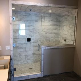 A large white marble tiled shower enclosed by sleek glass doors. The pristine white marble tiles exude a sense of luxury and sophistication, while the glass doors add a touch of modern elegance, creating an inviting and stylish shower space.