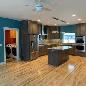 Dark wood cabinets, granite counters and backsplash, stainless steel appliances, and white pine floors define this kitchen. The vibrant blue-green walls add a refreshing pop of color, creating a captivating and stylish culinary space.