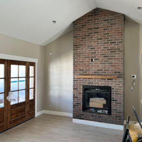 Brick propane fireplace with peaked ceiling. Adjacent walnut door opens to outside, combining rustic charm with natural elegance.