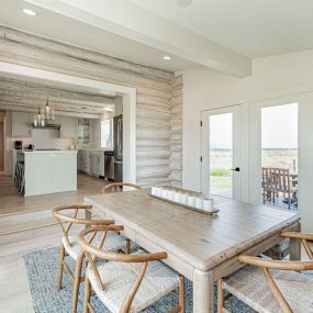 Bright dining room addition to log cabin with white oak floors, offering a seamless view into the adjacent modern kitchen. The combination of natural light, rustic elements, and contemporary design creates an inviting and harmonious space.