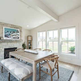 A bright white dining room adorned with white oak floors and a captivating white stone fireplace. The large windows flood the space with natural light, creating an airy and inviting atmosphere. A blend of elegance and comfort in a log cabin setting.