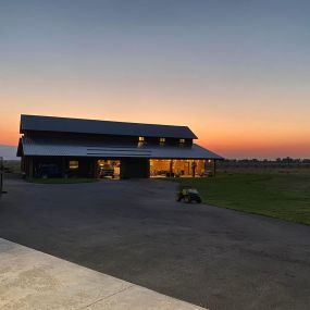 A newly completed large barn-style shop/garage with open doors, showcasing a beautiful sunset. The shop features elegant cedar siding, adding a touch of rustic charm to the structure.