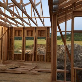 New home with completed framing, plywood walls, and mountains in the background. Clean construction site.