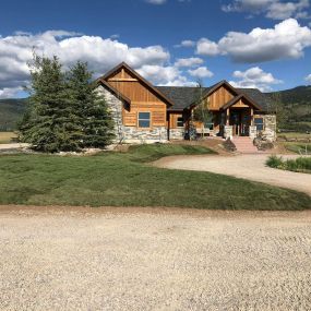 Newly completed modern Western home with wood and stone siding, beautiful landscaping, and mountains in the background.