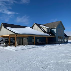 Newly built house with blue siding, high peaked roof, oversize 2-car garage, motor home parked outside, snow on the ground, and blue skies.