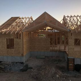 New home under construction with framed walls and plywood installation in progress. Trusses are in place, awaiting the roof. The construction site is clean and well-organized, ready for further progress.