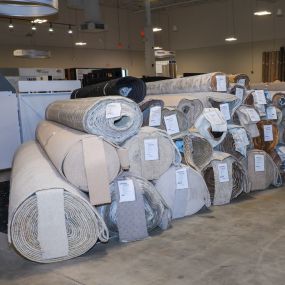 large stack of rolls of carpet in the middle of the USA Flooring store in Raleigh. The stack is made up of several rolls of carpet, each one tightly rolled up and stacked on top of the others. The carpet rolls are of different colors and textures.