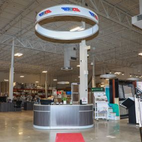 Interior of a USA Flooring store in Raleigh, with a variety of carpet and flooring options visible. A round white object with the USA Flooring logo is visible on the ceiling.