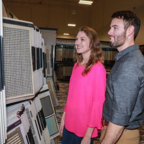 The image shows a man and woman standing in front of a display of carpet samples