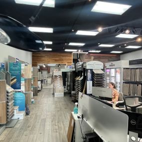 At USA Flooring Durham, a woman assists customers surrounded by a variety of flooring samples. With expertise and a diverse selection, customers can find the perfect flooring solution for their needs.