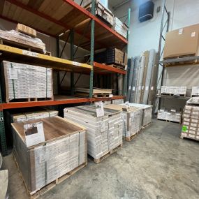 A warehouse scene captures neatly stacked pallets and boxes, containing various types of flooring products. The organized arrangement showcases the range of available flooring options, ready for distribution and installation.