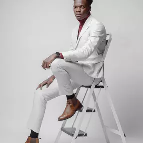 Sapien Designs Marketing Digital SEO created this image of a stylish man in a white suit and brown shoes sitting on a ladder.