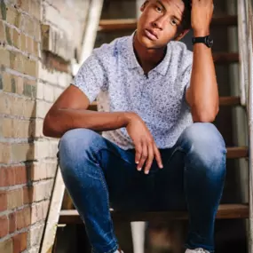 This image, developed and edited by Sapien Designs Marketing Digital SEO, features a person seated on stairs, wearing a patterned shirt, jeans, and white sneakers.