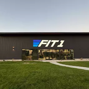 Steel Concepts Inc constructed a modern 12,600-square-foot steel-frame gym for Fit 1 in Twin Falls, ID. The sleek building showcases a durable and innovative design, featuring large glass windows and the Fit 1 logo prominently displayed on the facade, all against the backdrop of a serene sunset.