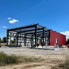 We're Building America recently completed a multi-use industrial steel frame building with an industry partner in Thornton, ID. The construction site features a partially completed structure with large red panels and visible steel framework