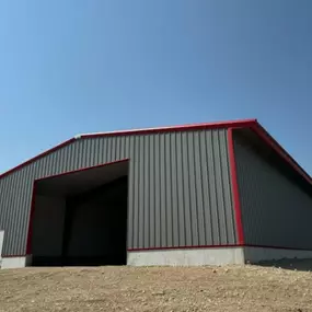 The building is constructed on a 2-foot concrete wall foundation, providing a solid and durable base. The structure includes a large open entrance and a smaller side door, making it versatile for industrial, agricultural, or commercial applications. The elevated position and surrounding terrain highlight the building's robust construction and adaptability, showcasing Steel Concepts' commitment to quality steel structures.