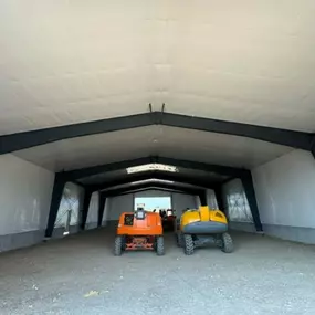 An interior view of a steel building under construction by Steel Concepts, showcasing the structural framework and progress. This image highlights the steel beams, white paneling, and the presence of construction equipment within the building. The gravel or dirt floor indicates the ongoing construction phase, emphasizing Steel Concepts' expertise in steel fabrication and building erection.