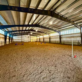 An interior view of the 10,800 SQFT riding arena in Idaho Falls, completed by Steel Concepts, Inc. Designed for optimal durability, safety, and year-round use, this facility features a high-strength, open-span steel frame providing ample column-free space. The image highlights the spacious, functional interior with a dirt riding surface and visible equestrian equipment, showcasing a high-performance space built for training, events, and recreation.