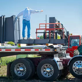 This image captures a crucial stage of construction logistics, showing a flatbed truck transporting significant steel structural components. These materials are intended for a Steel Concepts general contracting project, specifically a 12,600 square foot Regional Gym located in Twin Falls, ID, falling under the retail category. A worker is visible on the truck bed, appearing to direct or secure the load, highlighting the ongoing activity in preparing for the building's construction.