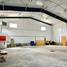 This image showcases the interior of a 2,500 sq ft airport hangar, a general contractor project by Steel Concepts. The space highlights Steel Concepts' insulation products, specifically the white curtain insulation covering the walls and ceiling, providing thermal regulation and a clean finish. The hangar is currently empty, with an open concrete floor and various equipment along the walls, indicating a functional and versatile space.