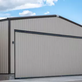 This image features a 2,500 sq ft airport hangar, a project by Steel Concepts. The building showcases their expertise in metal construction with a beige and dark brown exterior. A prominent element is the large fabric curtain door, a specialized product offered by Steel Concepts, designed for robust and efficient access for aircraft within this general contractor project.