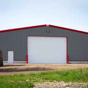 This image highlights a 7,200 sq ft shop building by Steel Concepts, constructed with their signature gray and red metalwork. A prominent feature is the large white roll-up curtain door, a key product by Steel Concepts, demonstrating efficient and robust access solutions for this general contractor project.
