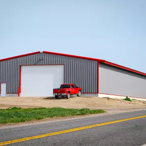 This image features a 7,200 sq ft shop building by Steel Concepts, highlighting their expertise in metal construction with gray siding and red trim. A prominent white roll-up curtain door, a key product by Steel Concepts, is centrally visible, demonstrating efficient access solutions.