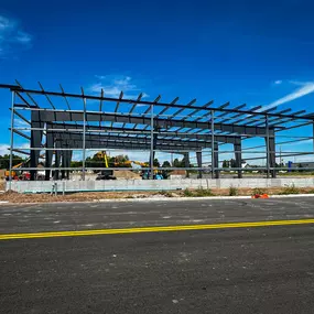 This image features a newly erected metal building frame by Steel Concepts, demonstrating the early stages of a robust construction project. The clear blue sky highlights the precise alignment of the structural steel beams and columns, which form the skeleton of the future facility. The building's foundation is clearly visible, providing a solid base for the pre-engineered metal structure.