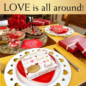 A Valentine's Day-themed table featuring Florence's Exquisite Chocolates in Rexburg, ID. The table is adorned with heart-themed plates, decorative candy bowls, and romantic touches like red roses and festive napkins. Boxes of Florence's chocolates, beautifully packaged in heart designs and ribbons, are the centerpiece, surrounded by an assortment of chocolate truffles and candies. This inviting and elegant setup highlights Florence's chocolates as the perfect gift for Valentine’s Day.