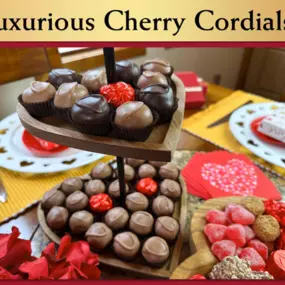 This image displays a variety of Valentine's Day-themed treats, likely from Florence's exquisite chocolates in Rexburg, Idaho.  The central focus is a two-tiered, heart-shaped wooden tray filled with heart-shaped chocolates. These chocolates are primarily light brown with darker brown accents, and a few are decorated with red accents.  On the table, there are also plates with white chocolate pieces, a red heart-shaped box, a small red envelope that says 