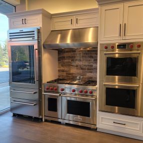 kitchen showroom with stainless steel ovens, range, and refrigerator on display