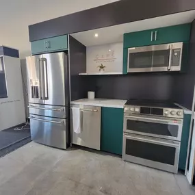 stainless steel refrigerator, dishwasher, range, and microwave on display with blue cabinets