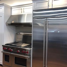 stainless steel fridge and range with hood on display with white cabinets