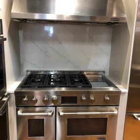 stainless steel range and hood on display with a white marble backsplash